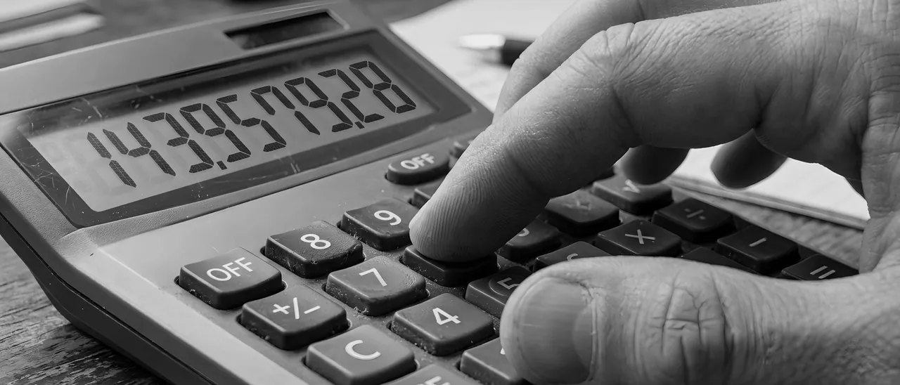 A hand pressing a key on a desk calculator, digits lit on its display.